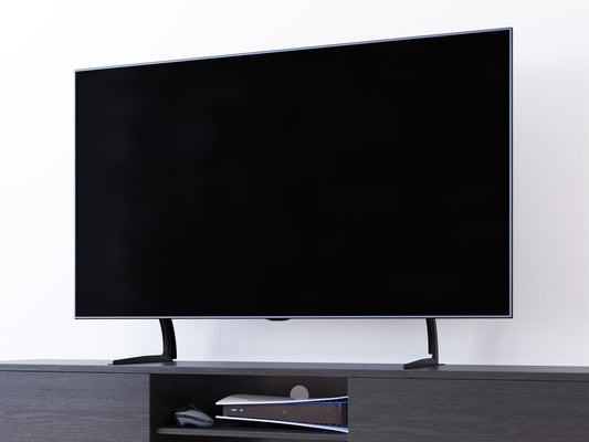 Modern black TV base stand with sleek metal frame, tempered glass shelves, and cable management system, suitable for TVs up to 70 inches. Contemporary design with sturdy construction and minimalist aesthetic.