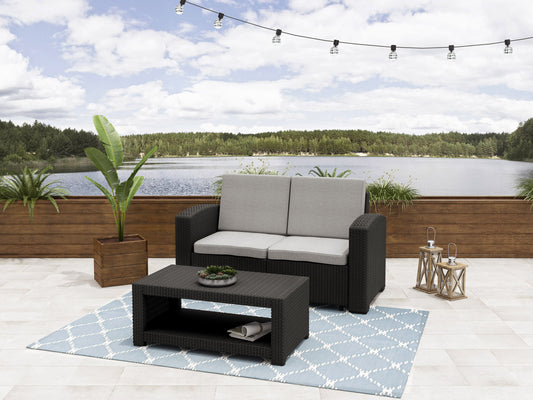Outdoor wicker loveseat in beige with plush white cushions, featuring a sturdy steel frame and weather-resistant materials, perfect for patio or garden seating.