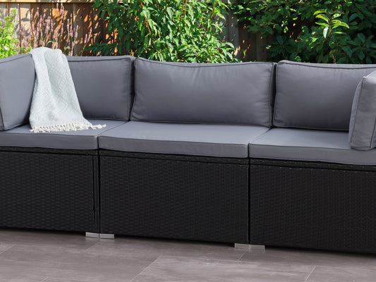 Gray wicker patio chair with beige cushions, featuring a high backrest and armrests, set on a wooden deck with green plants in the background. Ideal for outdoor relaxation and garden seating.