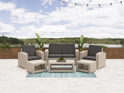 6 piece patio conversation set with beige cushions, dark brown wicker frame, glass-top coffee table, and matching ottomans, arranged on a wooden deck with greenery in the background.