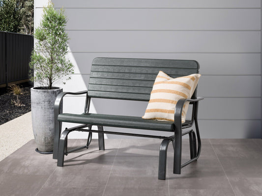 Gray metal gliding patio bench with curved armrests and slatted backrest, set on a wooden deck.