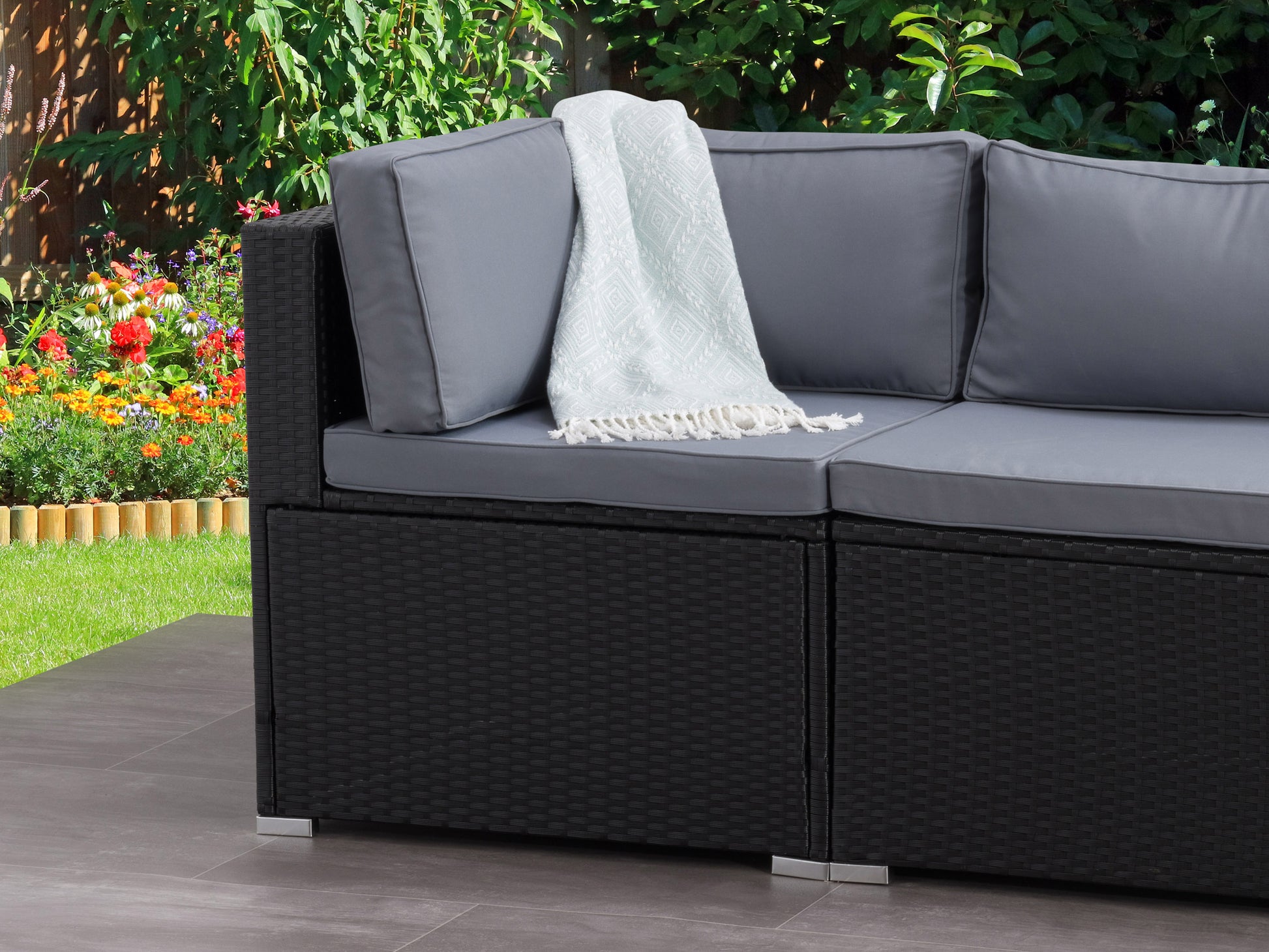 Outdoor corner patio chair with gray cushion, black metal frame, and wooden armrests, set on a wooden deck with greenery in the background. Perfect for stylish and comfortable outdoor seating.