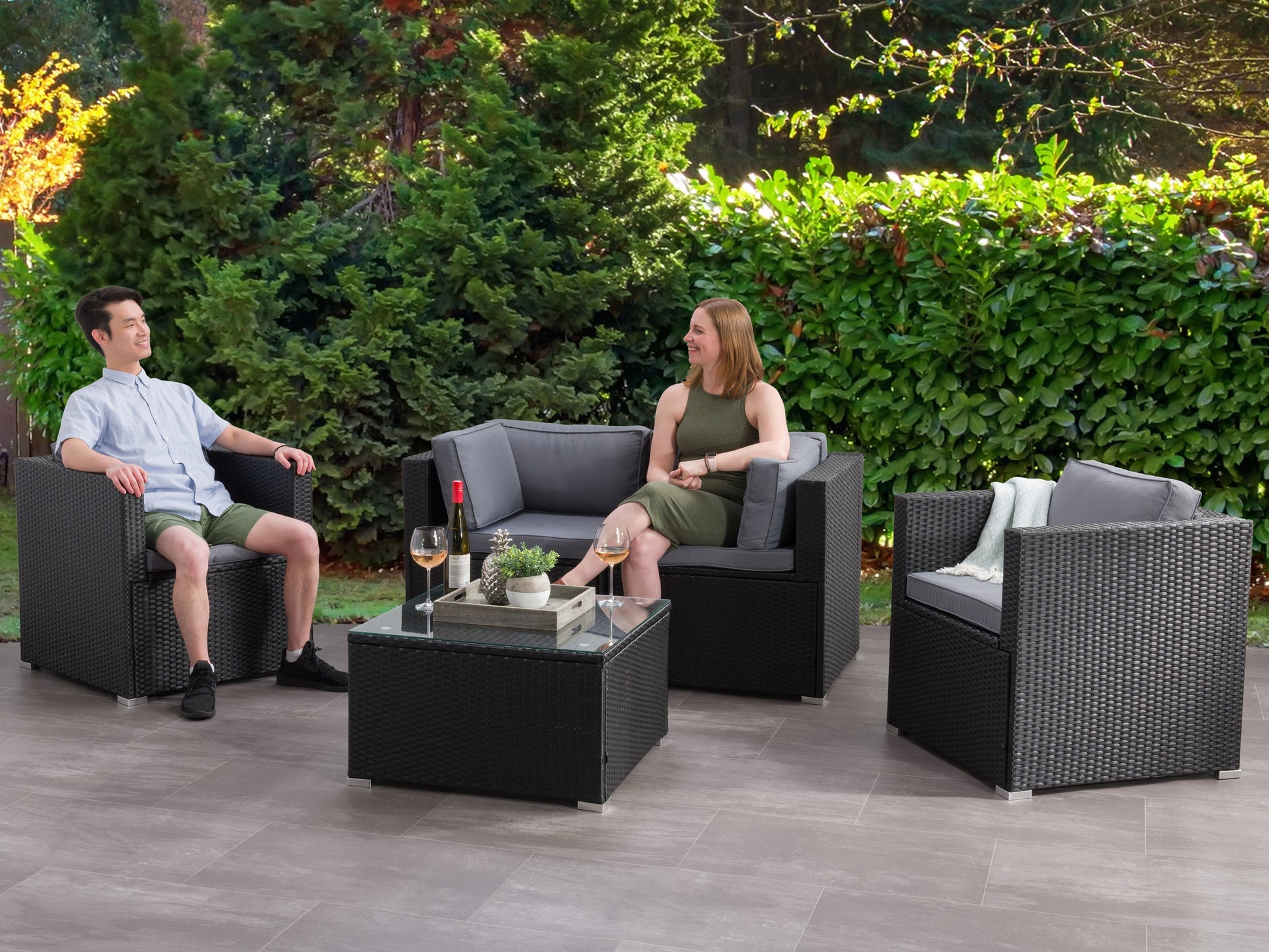Outdoor patio conversation set with a 5-piece sofa, featuring gray cushions, wicker rattan frames, and a glass-top coffee table, perfect for garden or backyard lounging.